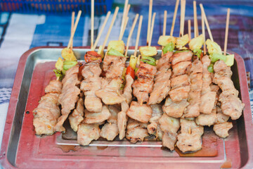 Grilled pork skewers on a tray, some with vegetables.