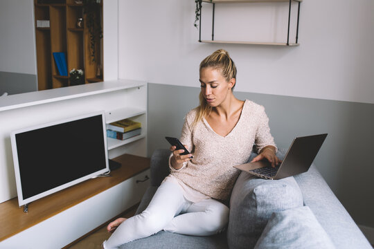 Focused freelancer multitasking with laptop and smartphone while working remotely from home, balancing mobile communication and digital workflow in a casual tech-driven environment