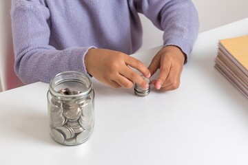 A little girl counting coins on the table. Learning to save money.