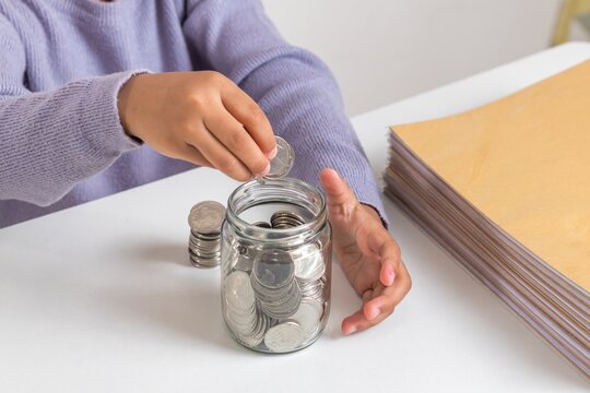 A little girl counting and putting coins into a glass jar. Learning to save money.