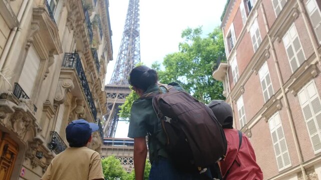 Family travelers &mdash; father and two children looking up at the eiffel tower from a paris street, surrounded by classic haussmann buildings on a sunny summer day exploring together