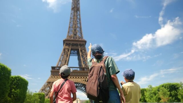 Family tourists from behind gaze up at the eiffel tower under a clear blue sky as a parent points the way, capturing summer vacation, exploration and bonding in paris