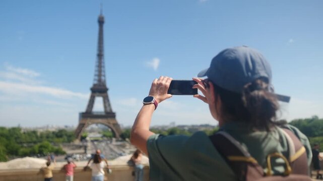 Woman tourist taking a picture of the eiffel tower with a smartphone on a sunny day in paris, enjoying city break travel and sightseeing experience