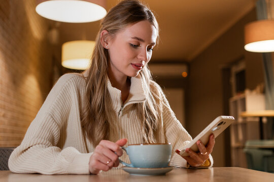 woman holding smartphone chatting in social networks using mobile applications sitting in modern cafe.