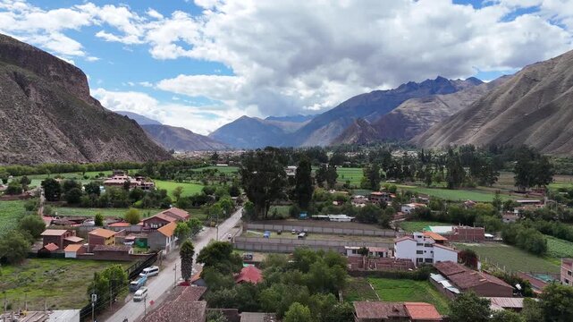 Aerial moving forward and raising over the town of Yucay, featuring green agricultural fields and the Andes Mountains in the Sacred Valley