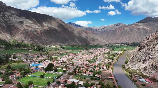 Aerial footage tracking the flow of the Urubamba River next to Yucay town, with the Andes Mountains and green agricultural fields surrounding the valley in Peru