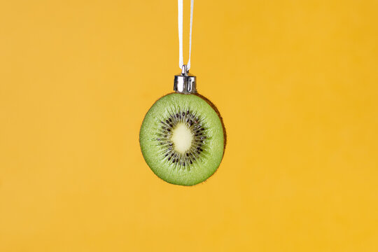 Creative christmas ornament: fresh kiwi slice hanging on white ribbon on yellow background