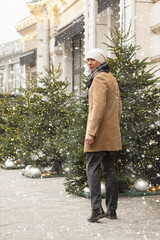 Adult caucasian man going to luxury store for shopping. Xmas holiday. Wearing warm clothing. Festive street with Christmas decorations.