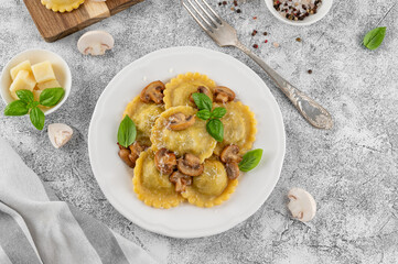 Tradition homemade Italian ravioli pasta with ricotta, mushrooms and parmesan cheese in a white plate on a concrete background. Top view.