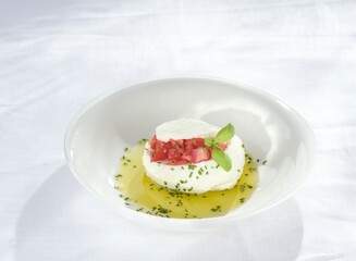 A creamy ball of mozarella is placed elegantly on a white dish, garnished with chopped tomatoes, olive oil, and fresh herbs. This simple yet refined dish highlights Italian flavors