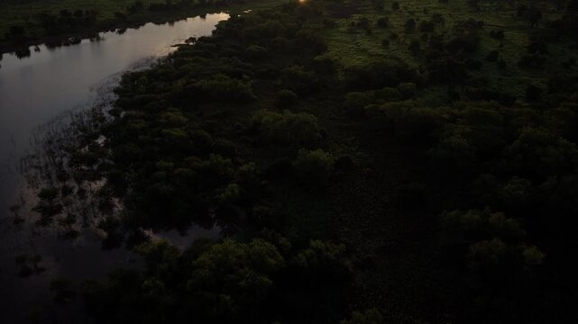 Aerial footage panning up over a dense rainforest and a river, revealing the city of Iquitos, Peru, against a beautiful sunset sky