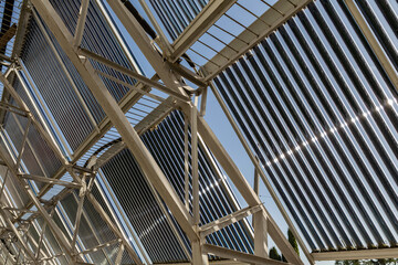 A low-angle view looking up at the metal support structure for a large installation of evacuated tube solar water heater collectors. Sunlight glints off the panels highlighting clean energy innovation