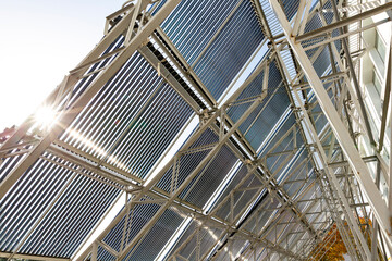 A low-angle view looking up at a large installation of evacuated tube solar water heater collectors. The bright sun flares through the panels, highlighting the metal support structure.