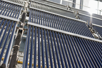 A close-up detail of an evacuated tube solar water heater collector system. The glass tubes are...