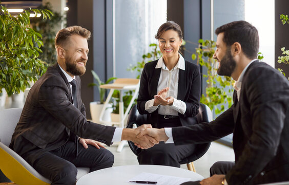Fototapeta Group of successful company employees making deal sitting in modern office. Happy smiling business people in formal clothes shaking hands on meeting. Teamwork and partnership concept.