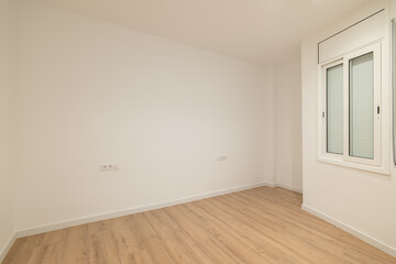 Empty room with white walls and wooden flooring. A single window allows natural light to enter. The space is minimalistic and ready for decoration.
