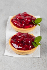 Two Cherry tartlets. With custard and mint. On serving paper