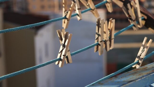 Clothespins hanging on a blue clothesline. The background is blurred, showing a hint of a domestic setting. The scene conveys a sense of everyday life and simplicity.