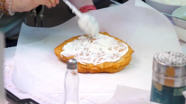 Hands carefully seasoning Krumplis Langos with sour cream and cheese