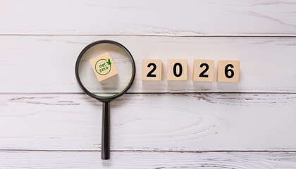 Green Net Zero Icon Under Magnifying Glass with Wooden Blocks Showing 2026