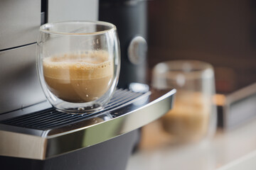 A modern double wall coffee cup with fresh milk coffee stands beside a stylish automatic machine creating a clean bright minimal lifestyle scene suitable for beverage marketing and cafe concepts use