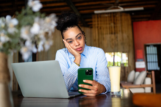 African american woman with a phone and laptop in a cozy space feeling unengaged while waiting
