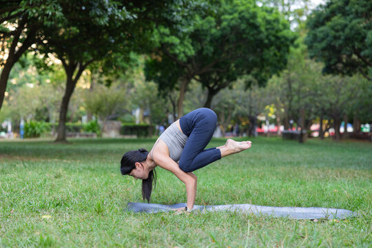 Woman practicing bakasana yoga pose outdoors park