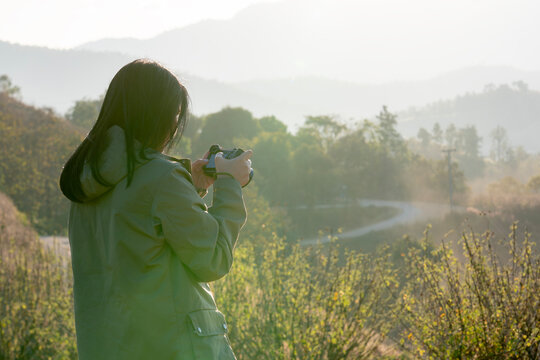 Rear view of a female tourist taking photos of a beautiful sunset on a mountain peak during the cold winter season. Concept of travel, adventure, freedom, and connection with nature.
