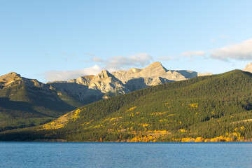 Autumn forest and sunlit peaks over lake in Alberta, Canada

