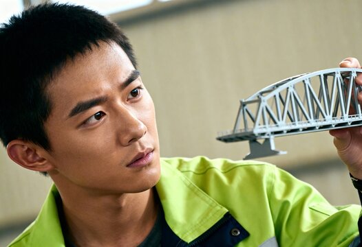 Young Asian engineer inspecting a scale model of a bridge. Professional architect focused on a construction project. Infrastructure design and development concept