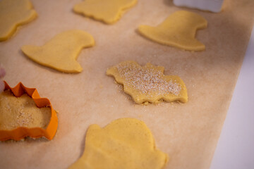 Close-up of a person preparing homemade cookies using Halloween-themed cutters. The hand sprinkles sugar on shaped dough pieces placed on parchment paper, ready for baking.
