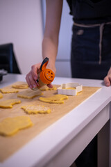 Close-up of a person preparing homemade cookies using Halloween-themed cutters. The hand sprinkles sugar on shaped dough pieces placed on parchment paper, ready for baking.