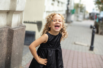 Fototapeta premium Little girl in a black dress joyfully playing in a charming city street on a sunny day
