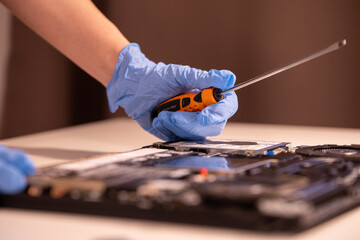 Technician wearing blue gloves using a screwdriver to repair or assemble a laptop’s internal...