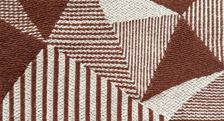 Close up of brown and white knitted fabric material in random stripes and geometrical triangular shapes pattern. For fabric, wallpaper, covering, and upholstery. Seamless background texture.