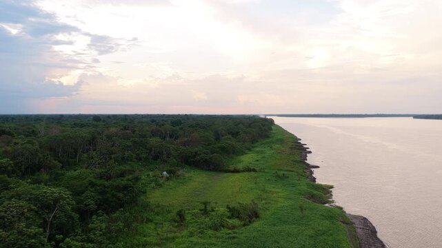 Small village bordering the vast Amazon river under a dramatic cloudy sky. Aerial shot highlighting the dense jungle and humble dwellings