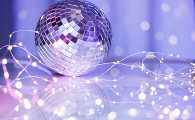 Silver disco ball with fairy lights on a reflective surface and bokeh background. Festive holiday or New Year party concept with glowing lights, dance vibes, and celebration mood.