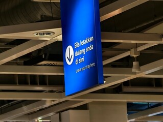 Low-angle view of a blue bilingual sign "Leave your tray here" hanging in a cafeteria.