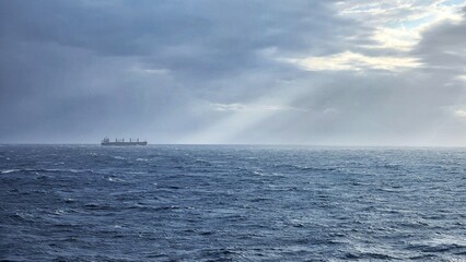 Cargo Ship in Open Sea under Dramatic Sky with Sun Rays