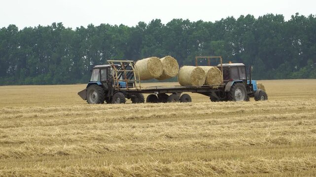 Tractor loading bales of hay on trailer.