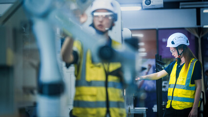 A female engineer in a hard hat and safety vest uses a tablet and stylus. She is focused, working in a high-tech smart factory or control room on a night shift.