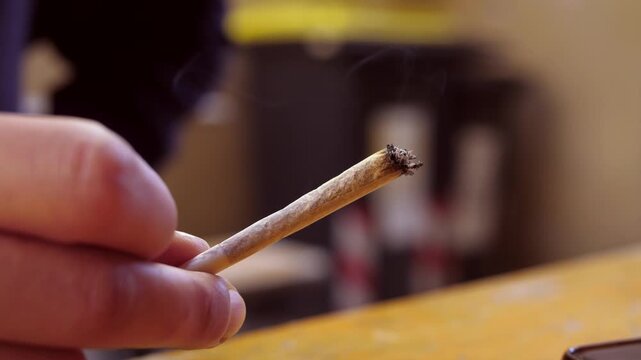 Lit cigarette held between young woman&rsquo;s fingers