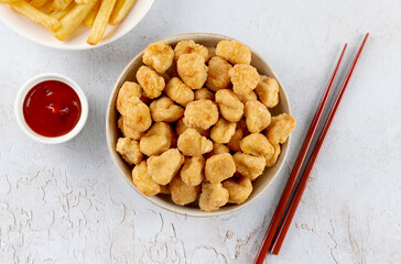 Crispy chicken popcorn with ketchup, French fries, and chopsticks on a white background. Top view. Fast food.