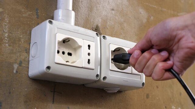 Detail of an electric plug being inserted into an aged wall outlet, showing the tactile and functional side of simple urban living.