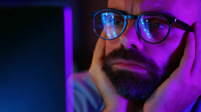 A focused individual gazes intently at a computer screen, marked by deep concentration and a hint of frustration, illuminating the challenges of digital engagement in modern work life.