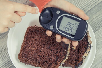 Hand of child holding glucometer with result sugar level, sweet chocolate cake. Nutrition during diabetes