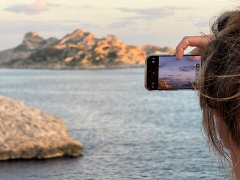 Woman capturing sunset ocean landscape with smartphone