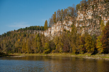 Discover the breathtaking Scenic Autumn Landscape that unfolds over a tranquil and calm River, surrounded by majestic Cliffs and lush Trees that showcase the beauty of nature at this vibrant season