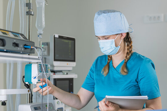 A nurse in scrubs checks an intravenous drip for a patient, showing attentiveness in a hospital setting.