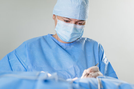 A skilled surgeon in blue scrubs and mask is concentrating while performing surgery in a bright operating room.